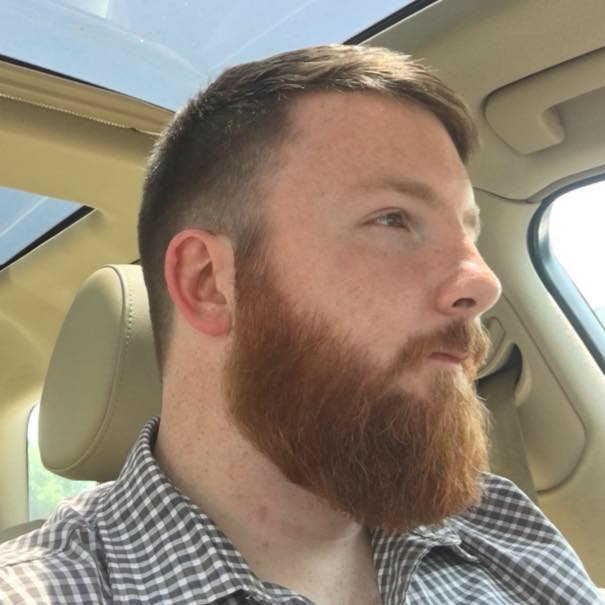 Picture of a man with a red beard in a car looking into the distance.